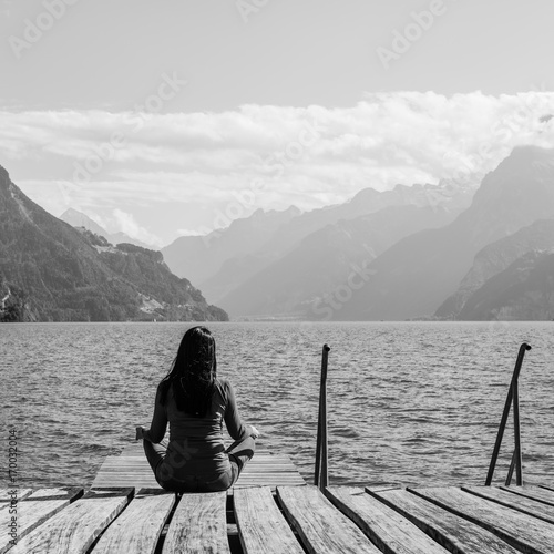 Meditation, self-reflection. Woman meditating sitting on the lake shore. Black and white.
