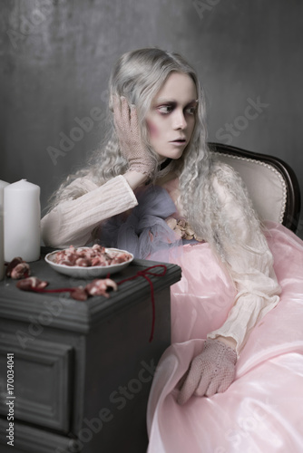 Dark halloween portrait of scary bad zombie girl sitting in a chair and collecting hearts. Conceptual photo