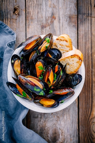 Delicious seafood mussels with with sauce and parsley.  Lemon and baguette . Clams in the shells.
