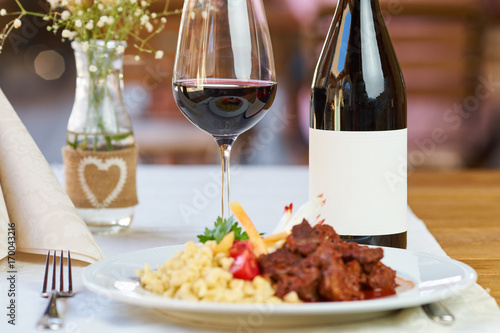 A bottle and glass of wine with food in a restaurant