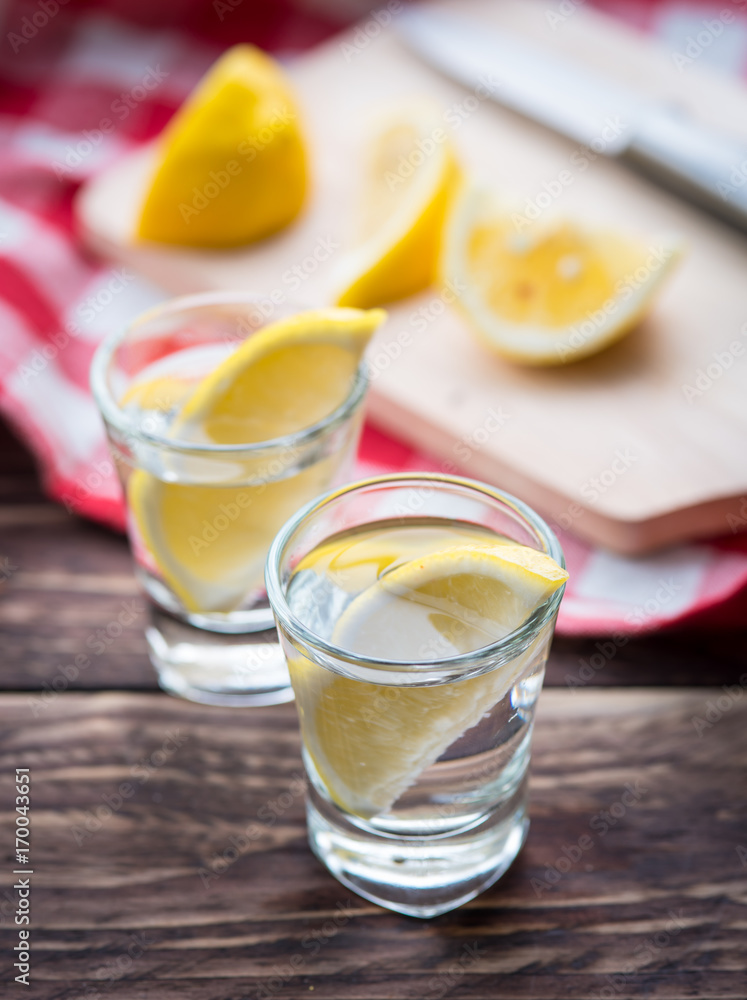 Vodka with lemon in shot glass on wooden background Vodka with lemon in shot glass on wooden background