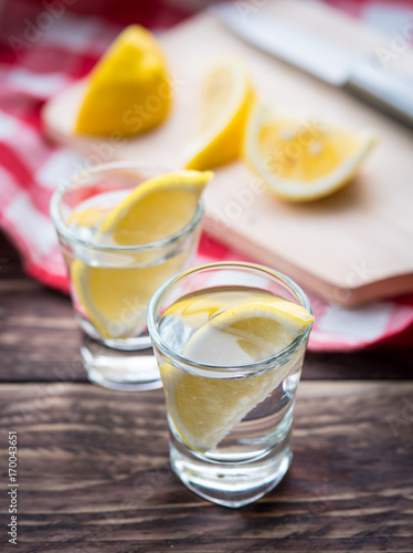 Vodka with lemon in shot glass on wooden background