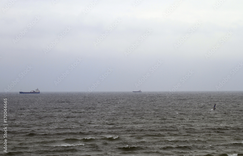 grey sky with two ships, kite surfer and waves in the sea