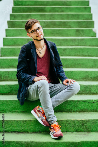 Portrait of a handsome teen student guy in glasses sitting on the green sairs - education, hischool and people concept. photo