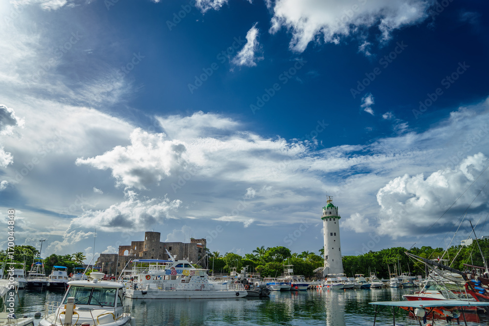 Many yachts and boats in the port on the background of a lighthouse and a beautiful sky