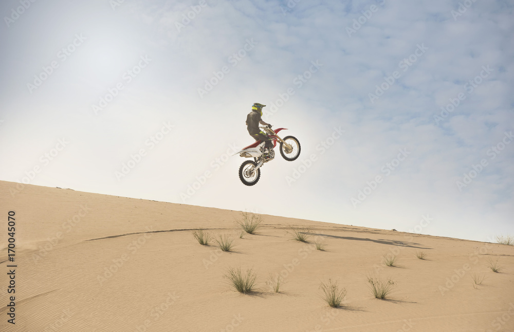 A dirt bike rider does an aerial jump in the desert sand dunes