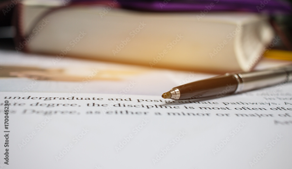 Blue metal pen on letter-writing paper book with letter about postgraduate or undergraduate degree in college or school with image of of hands writing article near textbook, concept of education Blue metal pen on letter-writing paper book with letter about postgraduate or undergraduate degree in college or school with image of of hands writing article near textbook, concept of education