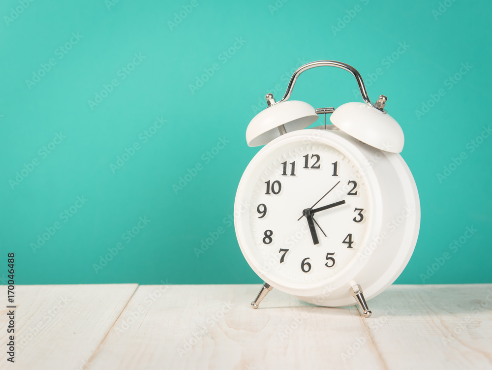 White old retro style alarm clock on wood table, mint green background White old retro style alarm clock on wood table, mint green background