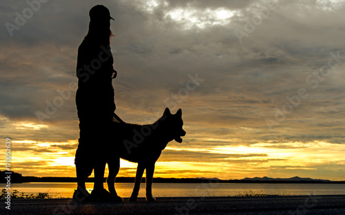 Silhoutte relaxed woman and dog enjoying summer sunset or sunrise over the river stand at near lake.  Lifestyle Concept