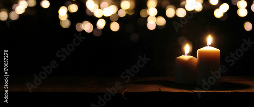 Burning candles over black background with bokeh glitter lights photo
