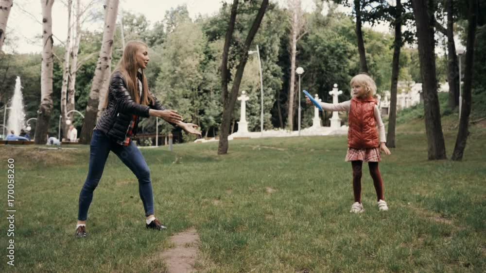 The little cute blond girl throwing a piece of a plastic shaped like a plate to the young pretty woman to catch as a game. Slow motion. HD The little cute blond girl throwing a piece of a plastic shaped like a plate to the young pretty woman to catch as a game. Slow motion. HD