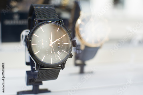 Close up of an beautiful black stainless steel watch. Beautiful watch in front of other watches. Lens flare in background.