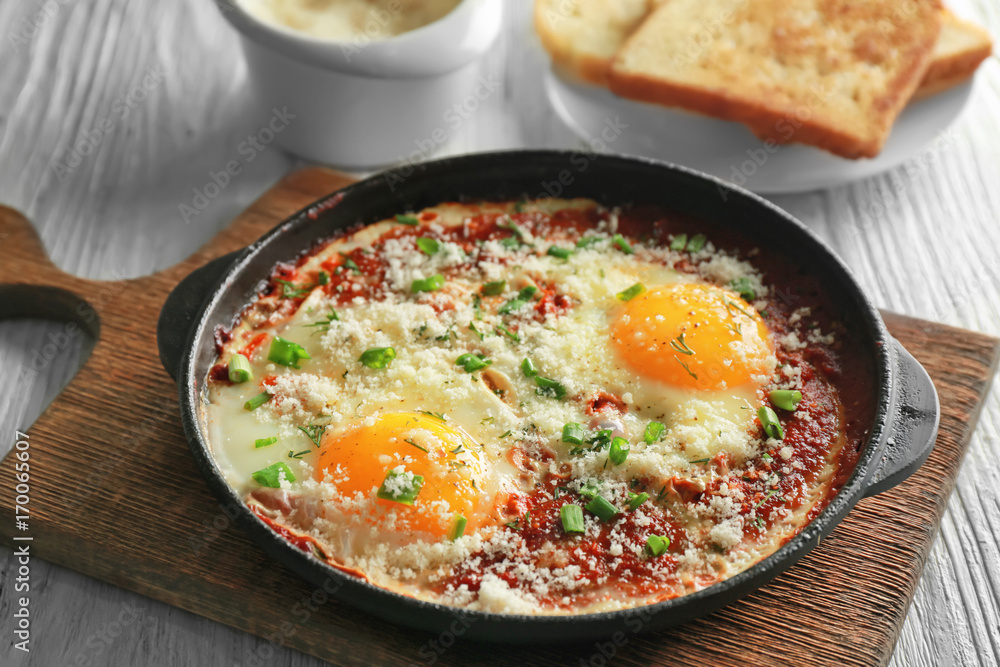 Frying pan with eggs in purgatory on wooden board Frying pan with eggs in purgatory on wooden board