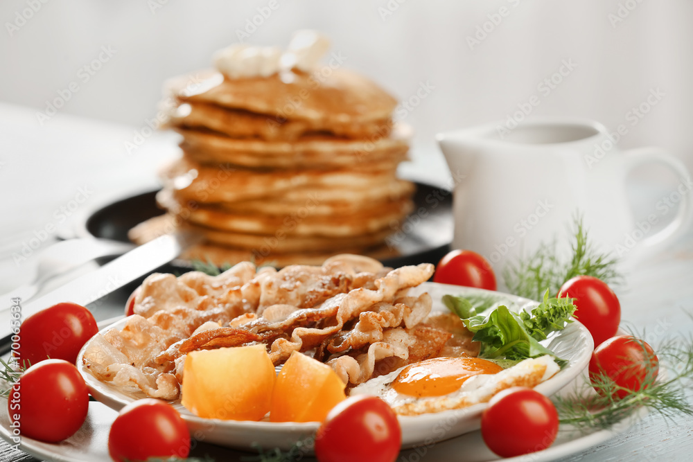 Tasty breakfast with fried egg, bacon and pancakes on table