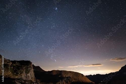 Night on the Alps under starry sky and the majestic rocky cliffs on the Italian Alps, with Orion constellation at the horizon.