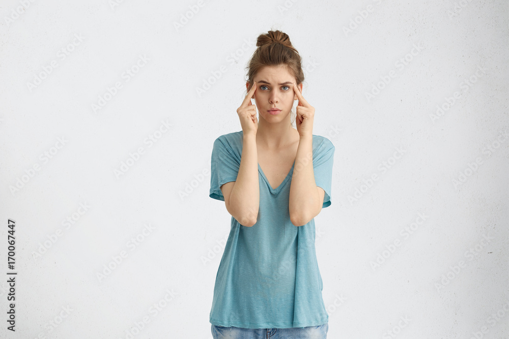 Portrait of thoughtful female trying to gather her thoughts, keeping fingers on temples, looking directly into camera with her blue warm eyes isolated over white background. People, lifestyle concept Portrait of thoughtful female trying to gather her thoughts, keeping fingers on temples, looking directly into camera with her blue warm eyes isolated over white background. People, lifestyle concept