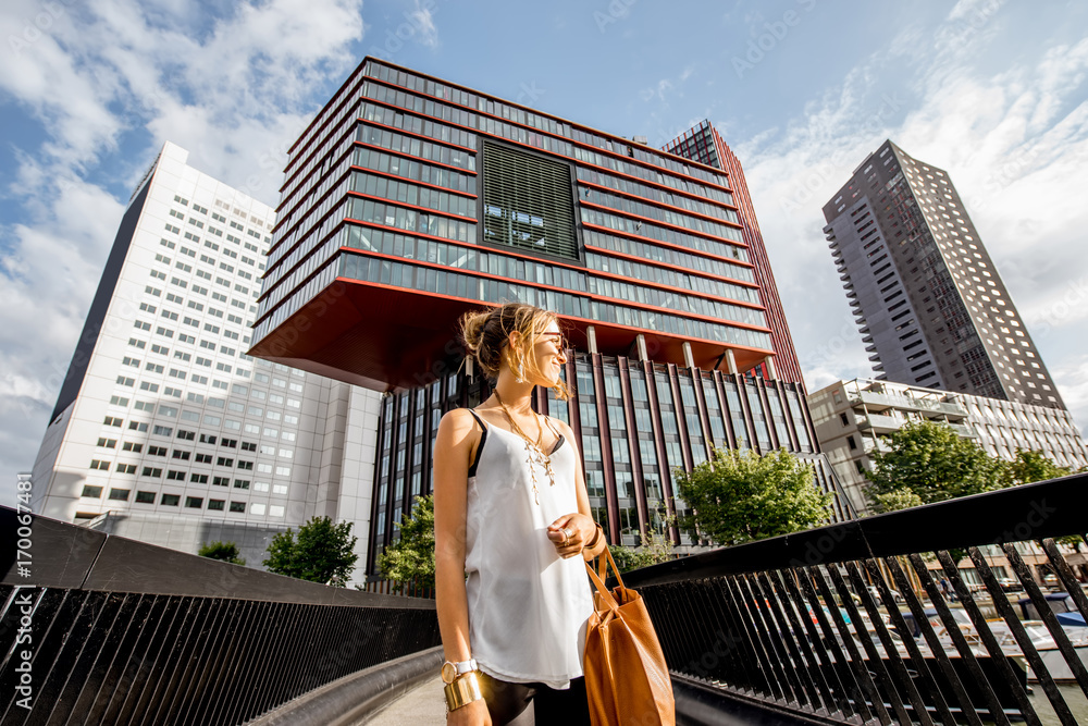 Lifestyle portrait of a young woman walking the bridge at the modern district with slyscrapers in Rotterdam city