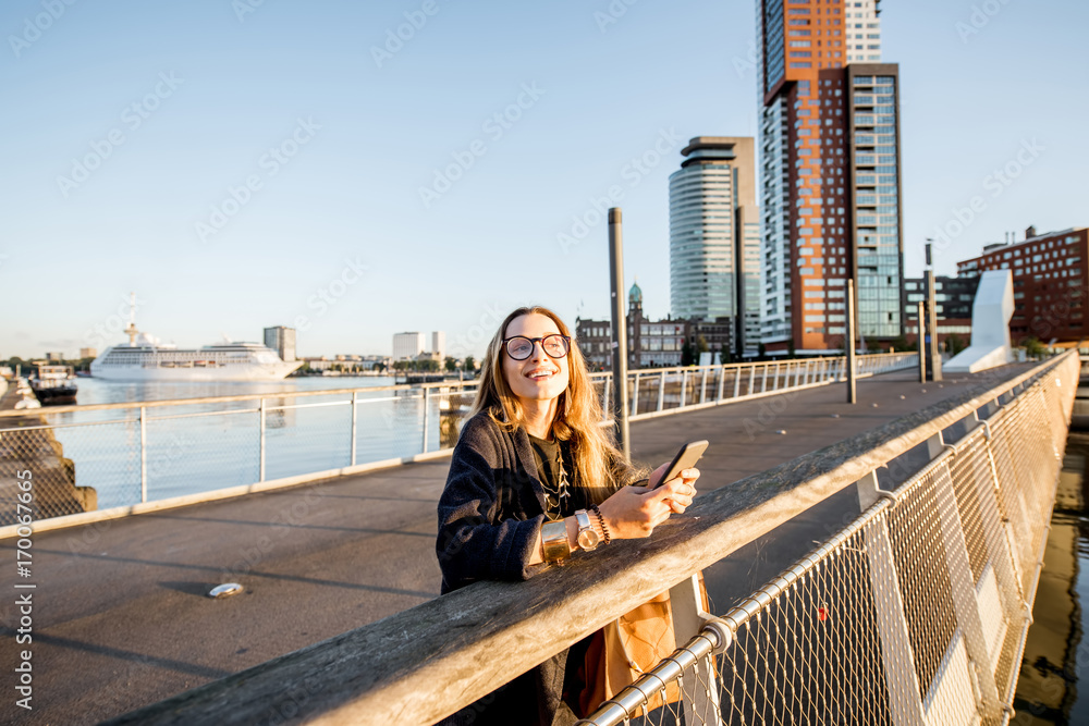 Woman standing with phone on the footbridge at the modern residential district during the morning in Rotterdam city Woman standing with phone on the footbridge at the modern residential district during the morning in Rotterdam city