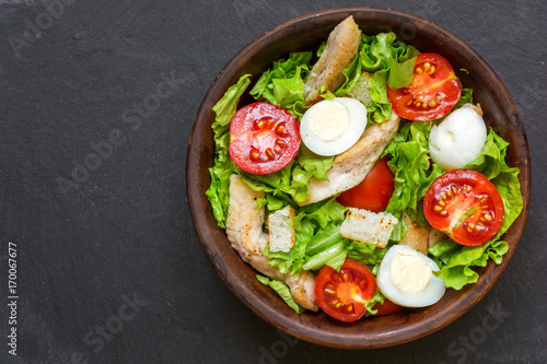 Caesar salad with croutons, quail eggs, cherry tomatoes and grilled chicken in a bowl