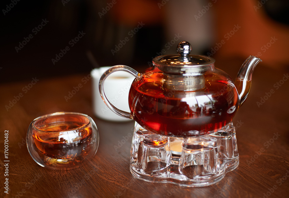 Glass infuser teapot with tea on the trivet and tea cup Glass infuser teapot with tea on the trivet and tea cup