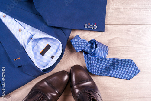 set of classic mens clothes - blue suit, shirts, brown shoes, belt and tie on wooden background.