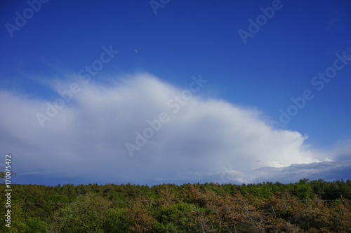 A huge fluffy cloud against the bright blue sky and moon