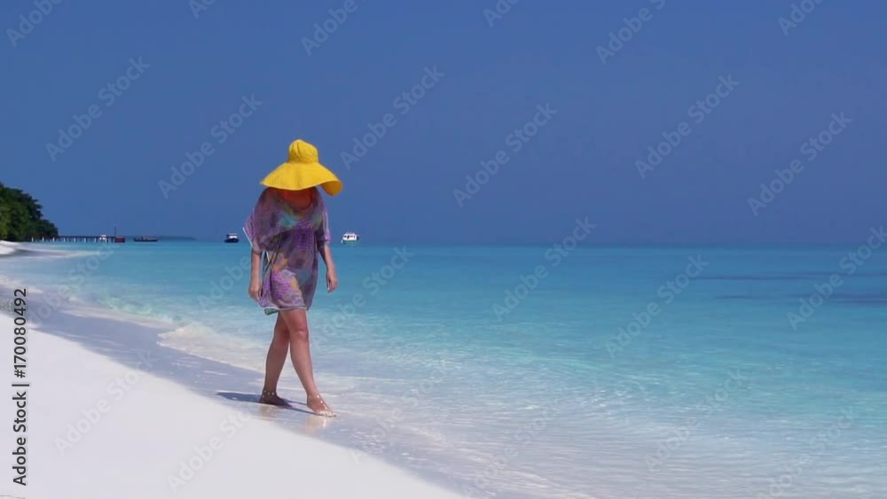 Woman in straw yellow sunhat walking along the beach with turquoise sea water Woman in straw yellow sunhat walking along the beach with turquoise sea water