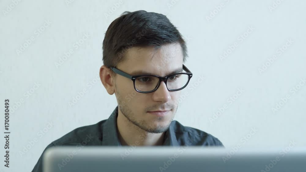 Portrait of a young man wearing glasses sitting in his office in front of a monitor - working on a computer. People stock footage slider shot. Portrait of a young man wearing glasses sitting in his office in front of a monitor - working on a computer. People stock footage slider shot.