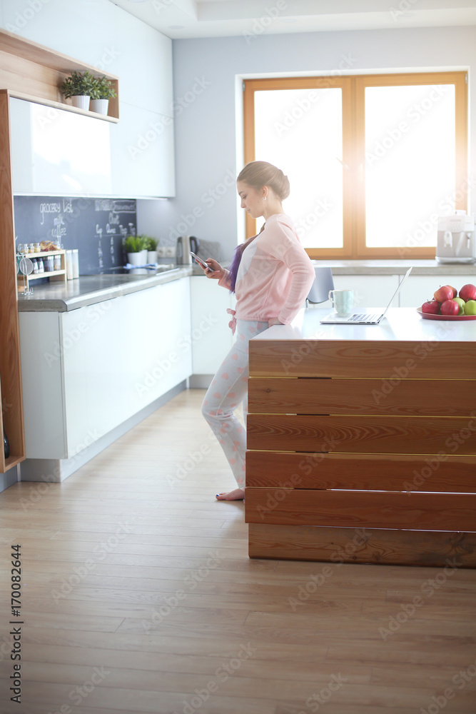 Woman using mobile phone standing in modern kitchen. Woman using mobile phone standing in modern kitchen.