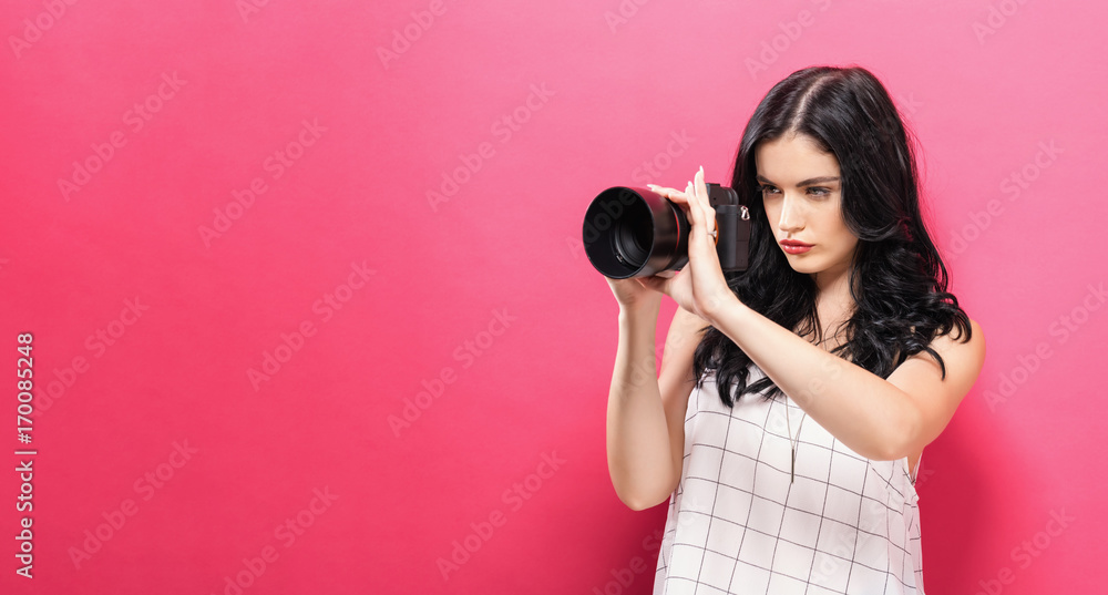 Obraz premium Young woman holding a camera on a pink background