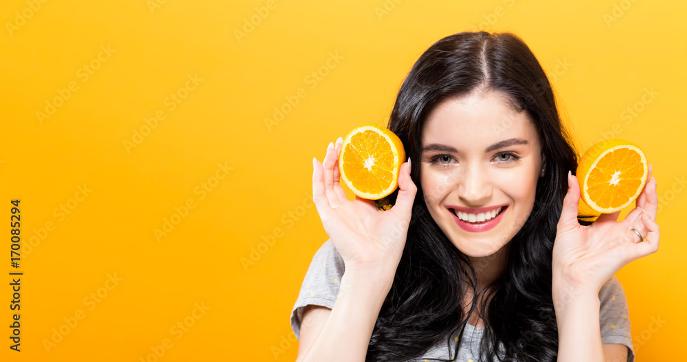 Happy young woman holding oranges on a yellow background Happy young woman holding oranges on a yellow background