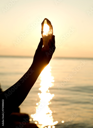 Young woman's hands holding clear quartz point in front of the lake sunrise photo