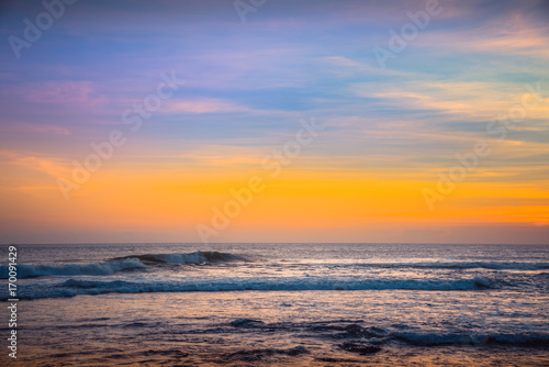 Colorful Background Sunset. Blue Waves near sea Resort. Sunset Background Ocean. Tropical Sunlight and Summer Sunset View. Isolated Sea Sunset. Surfing Beach with Surfers on the Horizon. Landscape © Irina