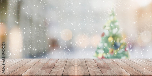 Wood table top on blur with bokeh christmas tree background with snowfall - can be used for display or montage your products