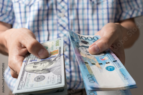 Photo of hands holding bundle of blue money in cash of one thousand philippines peso and US dollars as if being rich, boastful. Show off, pay bills or give bribe. Payment procedure