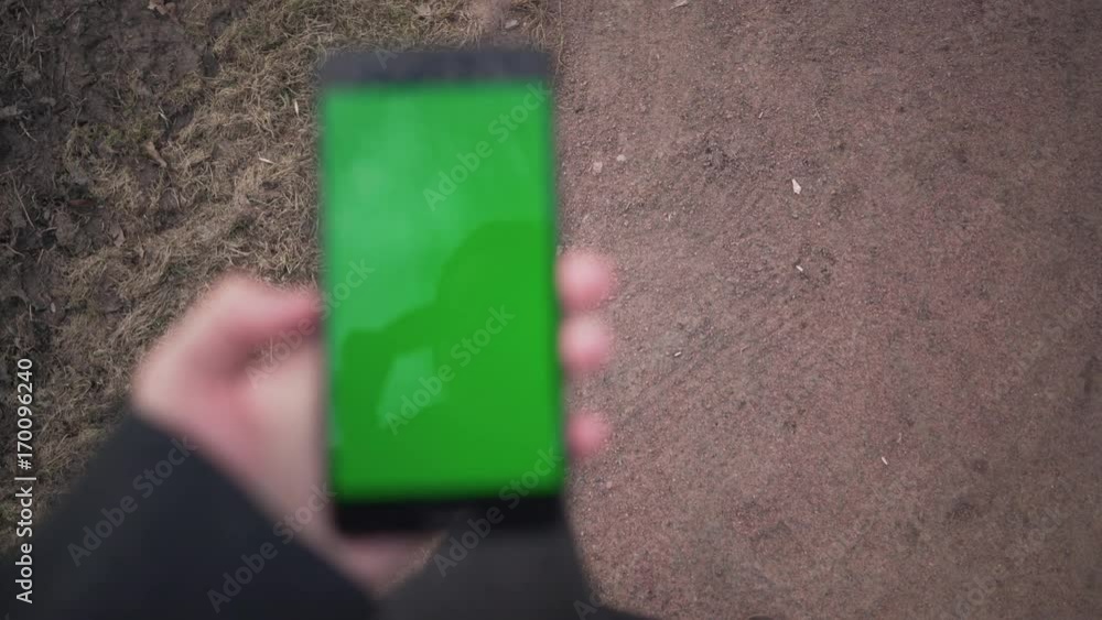 Handheld shot of man walking in town and holding smartphone with green screen pov view Handheld shot of man walking in town and holding smartphone with green screen pov view