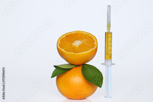 serum with vitamin C in a syringe and orange with leaves on a white background.