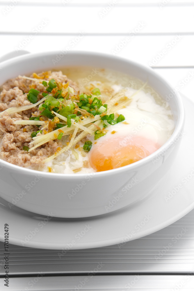 vertical pork chops rice porridge or congee with soft boiled egg and vegetable in the white bowl with spoon on the aluminium table for delicious breakfast and clean food in the morning vertical pork chops rice porridge or congee with soft boiled egg and vegetable in the white bowl with spoon on the aluminium table for delicious breakfast and clean food in the morning