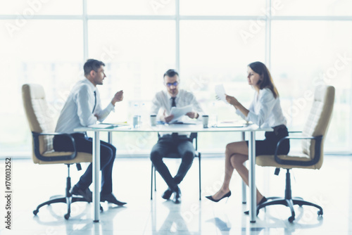 The three business people sit on the conference table