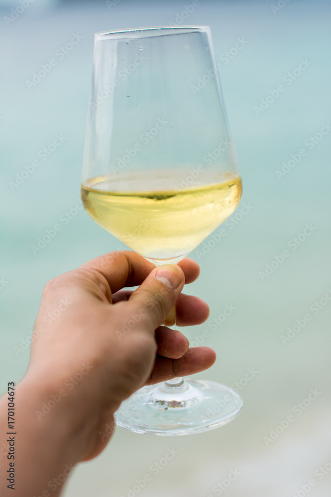 Obraz premium Hand holding White wine glass on beach background. Vacation and holiday travel for tourist in summer beach background.