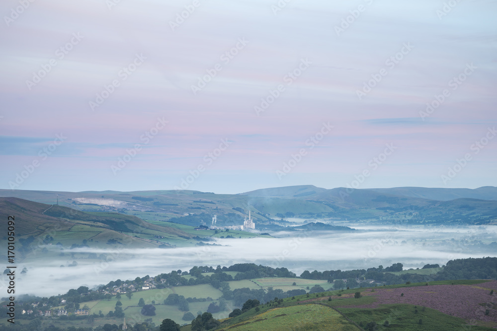 Beautiful dawn sunrise landscape image from Higger Tor towards Hope Valley layered in fog in Summer in Peak District England