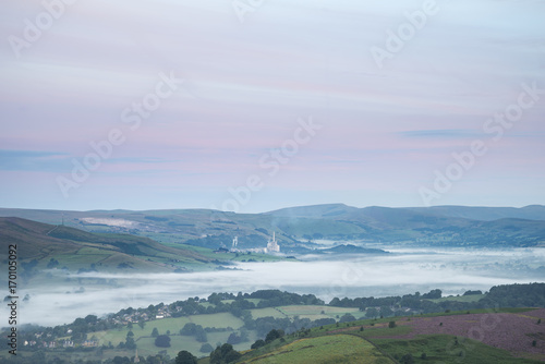 Beautiful dawn sunrise landscape image from Higger Tor towards Hope Valley layered in fog in Summer in Peak District England