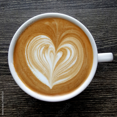 Fotografija Top view of a mug of latte art coffee on timber background.