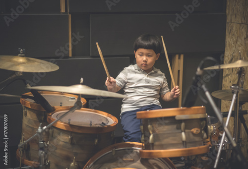 Little caucasian boy drummer playing the drum set in studio