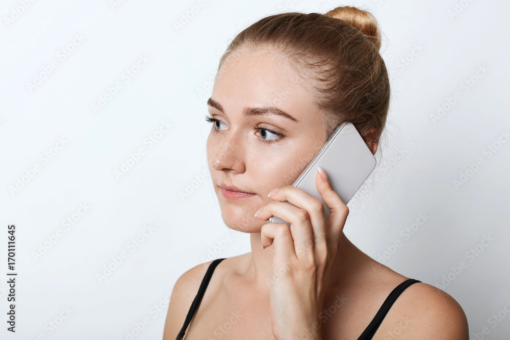 Close up portait of blonde female looking aside with serious expression while calling his friend or relatives, listening attentively something. Young attractive female chatting over mobile phone. Close up portait of blonde female looking aside with serious expression while calling his friend or relatives, listening attentively something. Young attractive female chatting over mobile phone.