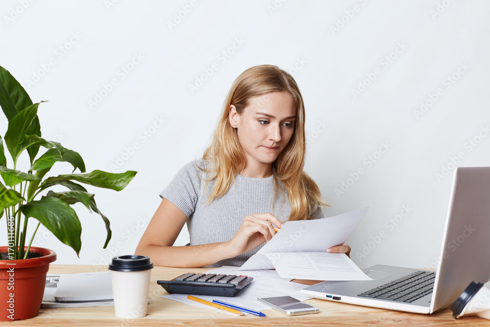 Portrait of young businesswoman working with laptop and calculator, looking attentively at documents, calcualting bills of company, making financial report. People, career and business concept Portrait of young businesswoman working with laptop and calculator, looking attentively at documents, calcualting bills of company, making financial report. People, career and business concept