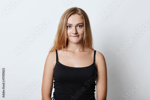 Horizontal portrait of beautiful young female with blonde hair, blue eyes and healthy skin, biting her lower lip while anticipating for important decision in life. People, facial expressions concept