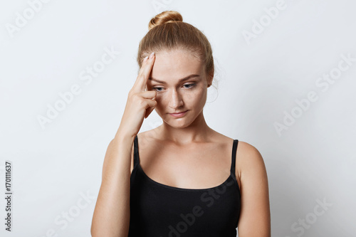 Thoughtful upset female with hair knot, having some problems in her life, thinking over how to solve them, looking down with unhappy expression. Beautiful woman with sad expression isolated on white