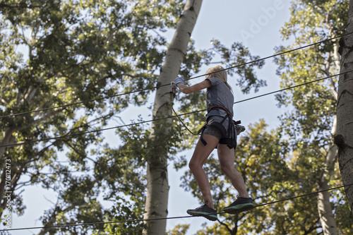Woman enjoying in a climbing adventure high wire park between trees. Challenge, accomplishment, success, breaking fear concept.