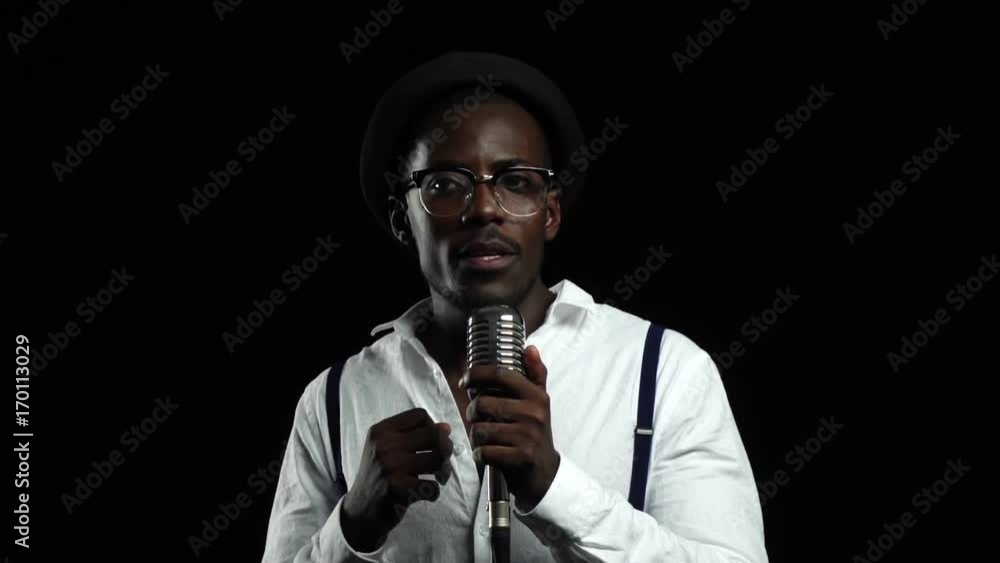 Man african american standing at the microphone professionally singing in a recording studio. Black background. Slow motion. Close up